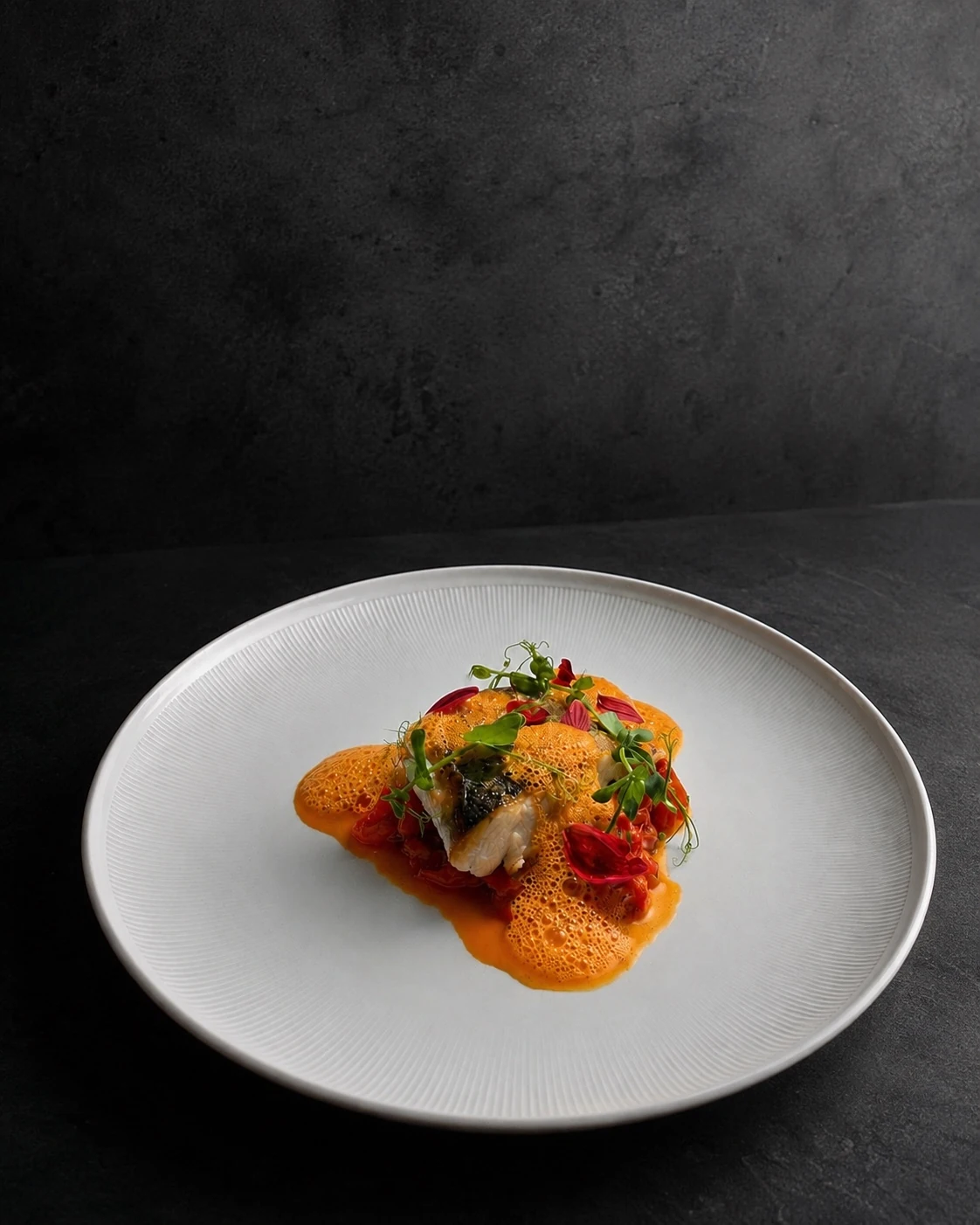 Assiette de poisson, émulsion orange et touches végétales, photographiée sur un fond sombre